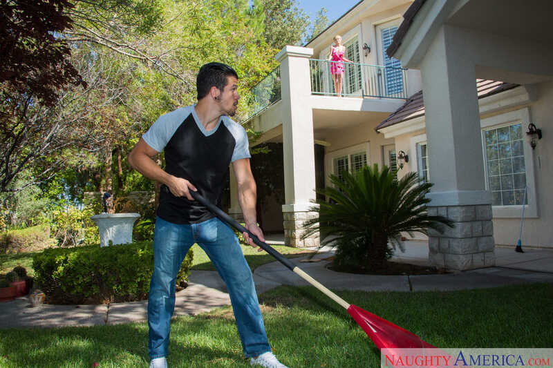 Scene from Naughty America Dee Williams porn video 'Dee Williams fucking in the bedroom with her tits' where Dee Williams is holding a red rake in the yard.