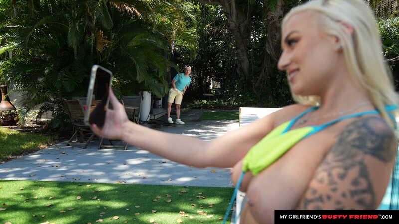 Scene from Naughty America Elana Bunnz porn video 'Elana Bunnz gets her big natural tits oiled up and  her pussy stuffed by friend's boyfriend' where Elana Bunnz is taking a selfie in front of a man in a lawn chair.