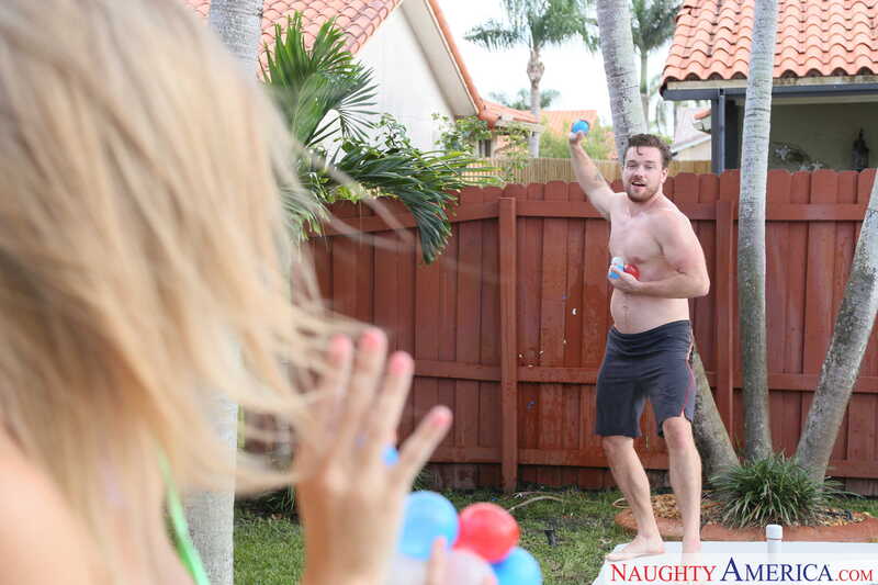 Scene from Naughty America Addison Lee porn video 'Ballbuster Addison Lee soothes and sucks them, too' where Addison Lee is throwing a ball at a man in a backyard.