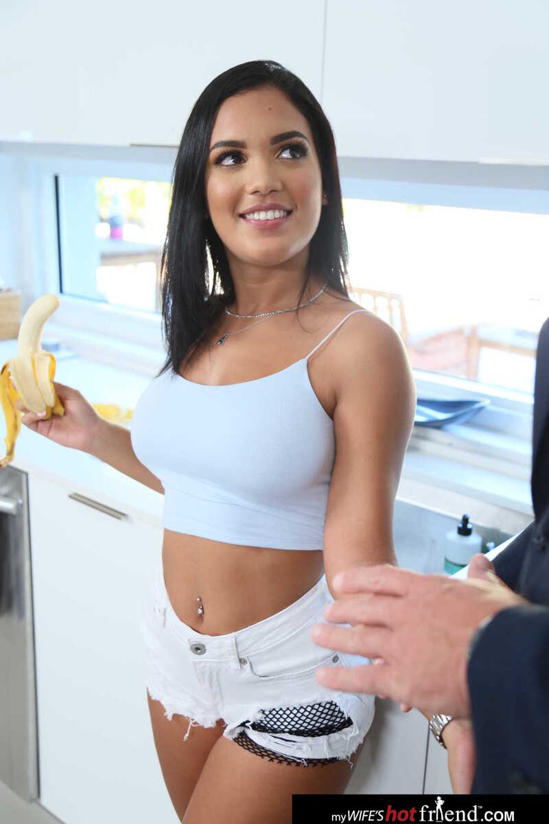 In the Alina Belle Naughty America porn scene 'Alina Belle takes a big dick from her friend's husband' from My Wife's Hot Friend, Alina Belle is wearing a crop top and shorts while holding a banana.