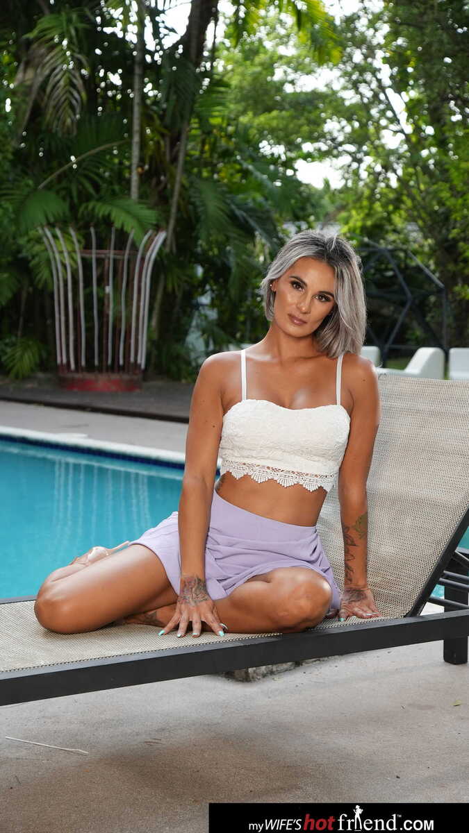 Scene from Naughty America Mandy Rhea porn video 'Busty blonde Mandy Rhea fucks friend's boyfriend's big  cock on vacation' where Mandy Rhea is posing in a white crop top and purple shorts.