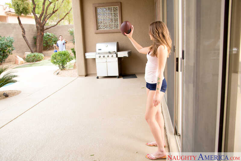 Scene from Naughty America Liza Rowe porn video 'Neighbor Liza Rowe fucking in the floor with her petite' where Liza Rowe is holding a football in her hand.