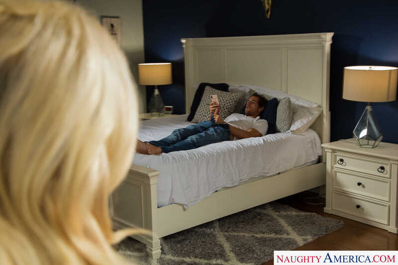 Scene from Naughty America Khloe Kapri porn video 'Watch slutty Khloe Kapri fuck her step brother' where Khloe Kapri is looking at a man laying in bed reading a magazine.