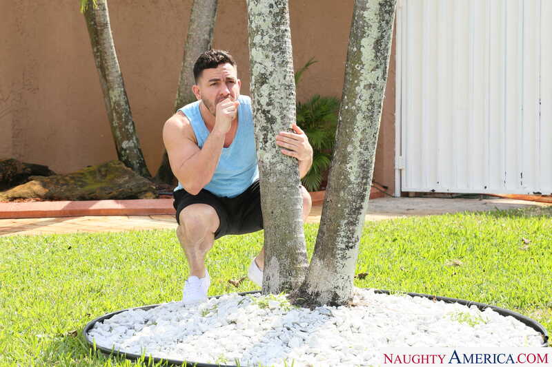 Scene from Naughty America Vina Sky porn video 'Vina Sky Rides Her Stepbrother's HUGE Cock' where Vina Sky is squatting behind a tree in a grassy area.