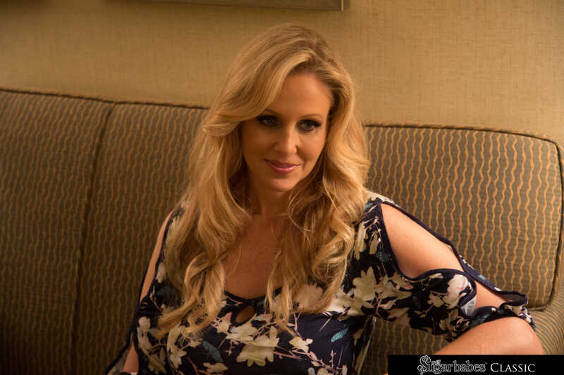 Naughty America Julia Ann porn: Julia Ann is sitting on a couch in a floral top.