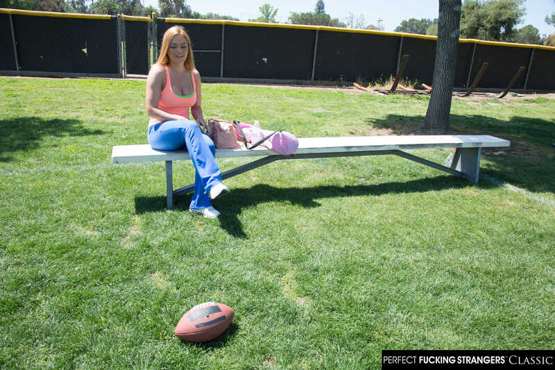 In the Krissy Lynn Naughty America porn scene 'Krissy Lynn gets her wet pussy fucked by a stranger' from Perfect Fucking Strangers, Krissy Lynn is sitting on a bench with a football in the grass.