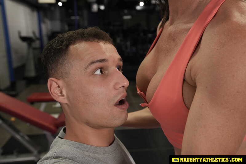 Scene from Naughty America Riley Jacobs porn video 'Sexy and fit Riley Jacobs gives one wet workout on a big cock' where Riley Jacobs is shown in a gym with a woman in a bikini.