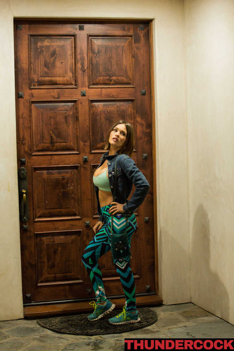 In the Krissy Lynn Thundercock porn scene 'Krissy Lynn fucks her bully's brother', Krissy Lynn is wearing a crop top and green pants in front of a door.