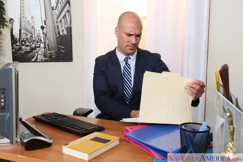 Scene from Naughty America Alex Blake porn video 'Alex Blake Gets Fucked In The Office' where Alex Blake is a bald man in a suit and tie.