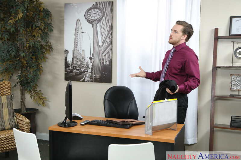 In the Dolly Leigh Naughty Office porn scene 'Super Blonde Dolly Leigh gets fucked in the office', Dolly Leigh is standing in front of a desk with a computer on it.